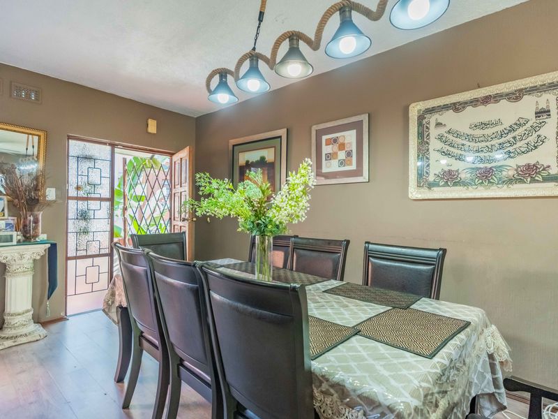 A dining room featuring laminate flooring, decorative pendant lighting, and direct access to the exterior through a security gate and timber door.