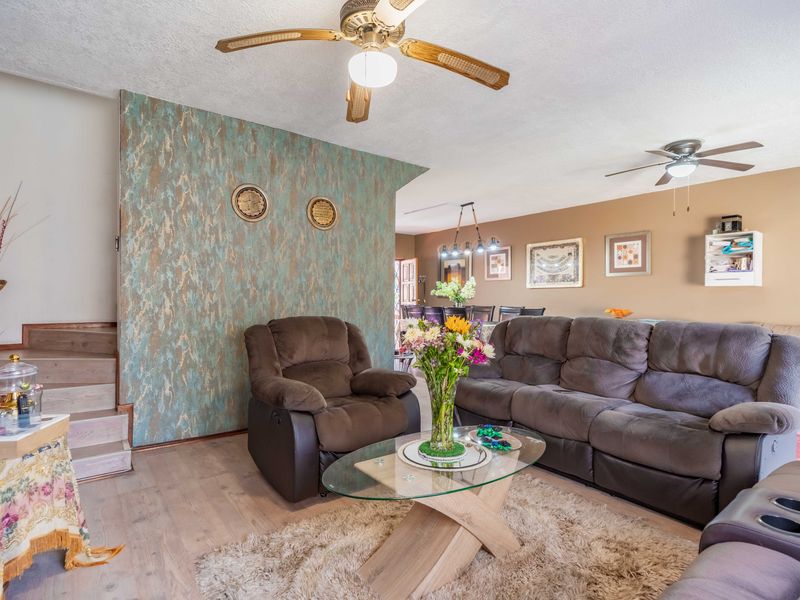 Open plan living and dining area featuring laminate flooring, ceiling fans, and a decorative feature wall with an adjacent staircase.