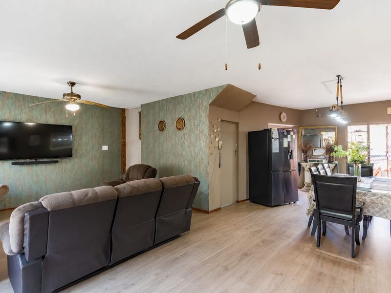 Open-plan living and dining area featuring laminate flooring, ceiling fans, and decorative wallpaper, creating a functional and connected living space.