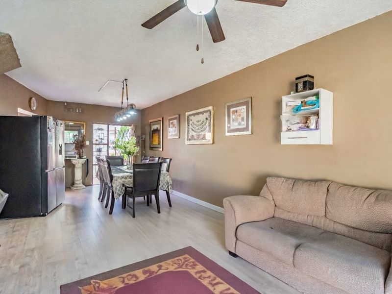 Open-plan living and dining area featuring light-toned laminate flooring, a ceiling fan, and direct access to the exterior through a security gate.