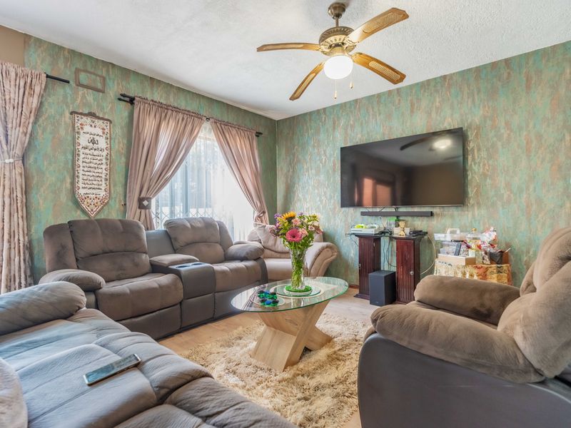 A living room featuring laminate flooring, a ceiling fan, and textured walls, providing a comfortable and functional space for relaxation.