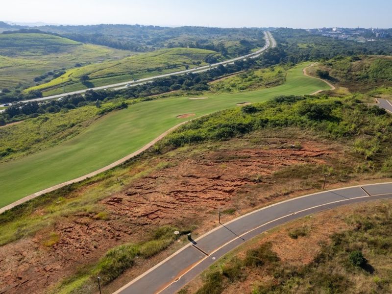 Aerial view of a vacant residential plot adjacent to a golf course and paved road infrastructure.