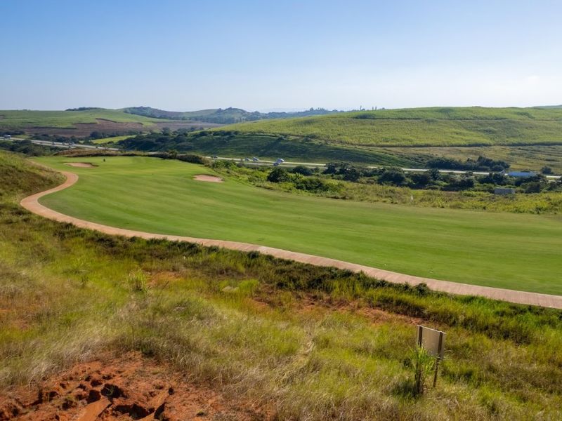 A scenic elevated view overlooking a well-maintained golf course fairway with a paved cart path and rolling green hills in the background.