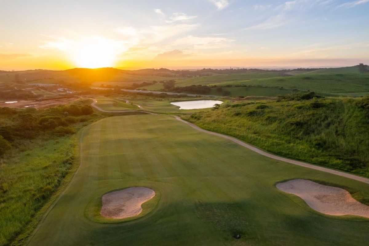 An aerial view of a well-maintained golf course fairway featuring sand bunkers and a water hazard at sunset.
