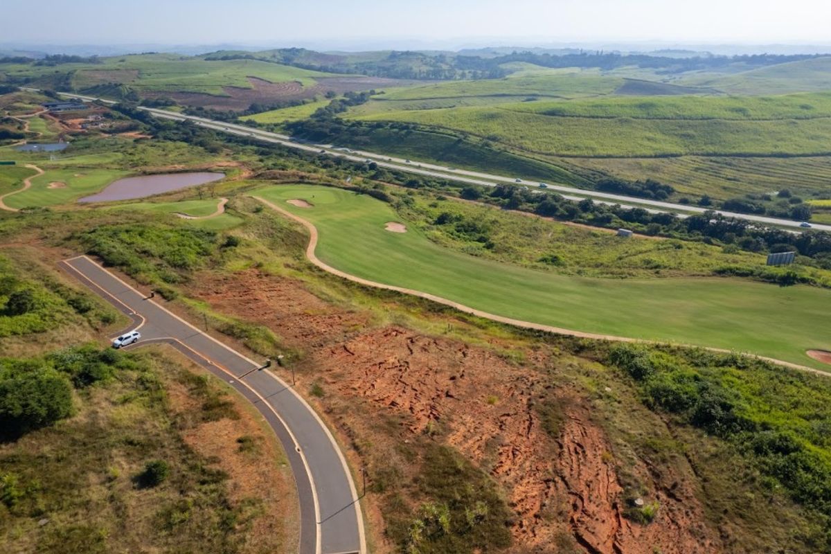 An aerial view of a vacant residential plot adjacent to a golf course, featuring paved road access and scenic landscape views.