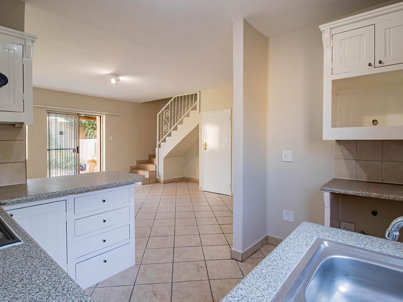 Open plan kitchen and living area featuring tiled flooring, built-in cabinetry, and a staircase leading to the upper level with access to a rear patio.