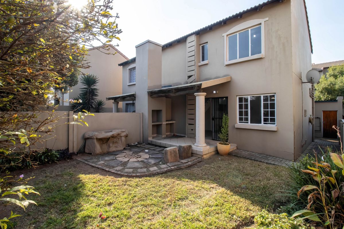 Rear view of the townhouse featuring a covered patio with a built-in braai, stone-paved seating area, and a private garden space.