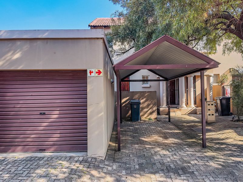 Front exterior view of the townhouse featuring a single roller garage door, a covered carport, and paved driveway area.