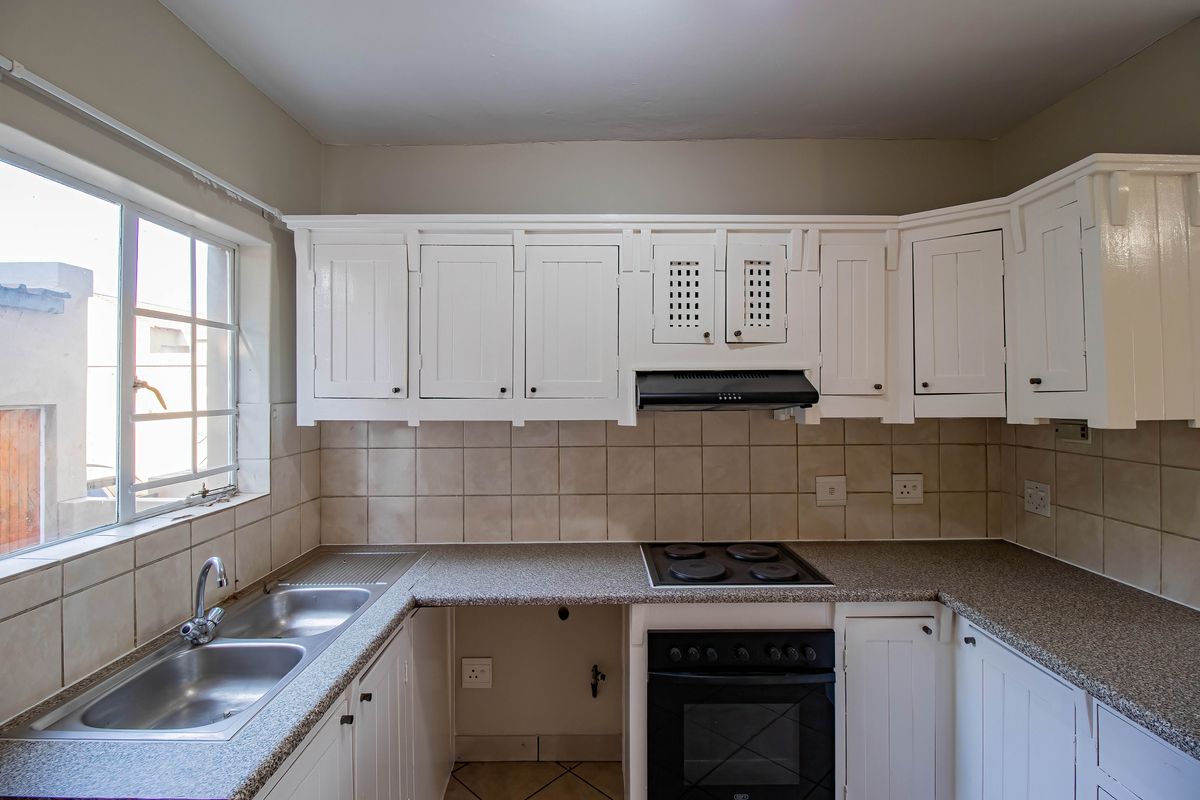 A functional kitchen featuring white cabinetry, granite countertops, a double basin sink, and built-in oven with extractor fan.