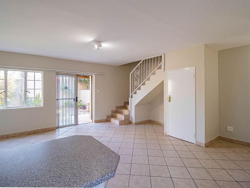 An open-plan living area featuring tiled flooring, a staircase with a metal balustrade, and direct access to an outdoor patio area.