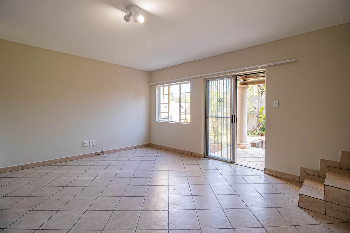 An empty, tiled living room featuring a sliding glass door with security gate, providing direct access to an outdoor patio area.