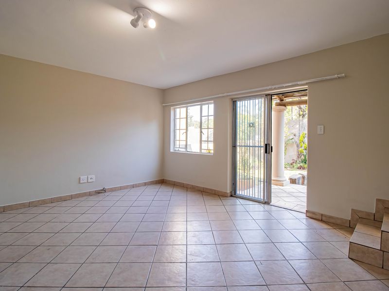 An empty, tiled living room featuring a sliding glass door with security gate, providing direct access to an outdoor patio area.