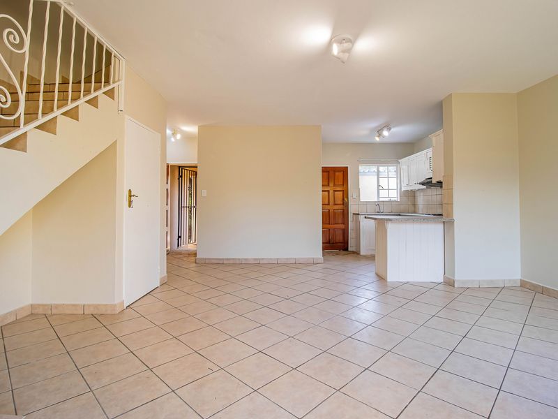 Spacious open-plan living area featuring tiled flooring, a staircase with a metal balustrade, and a functional kitchen with built-in cabinetry.
