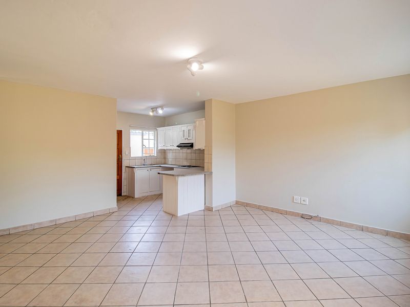 An open-plan living area featuring tiled flooring and a compact kitchen with white cabinetry, granite countertops, and a functional extractor fan.
