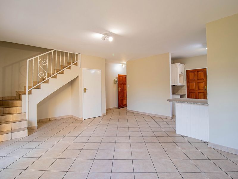 Spacious open-plan living area featuring tiled flooring, a staircase with metal railing, and a breakfast counter leading into the kitchen area.