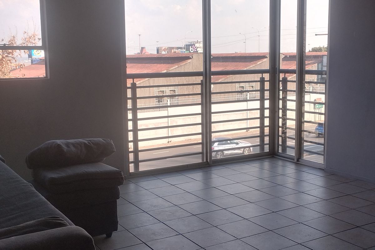An empty living area featuring tiled flooring and large glass sliding doors that open to a balcony with an urban view.