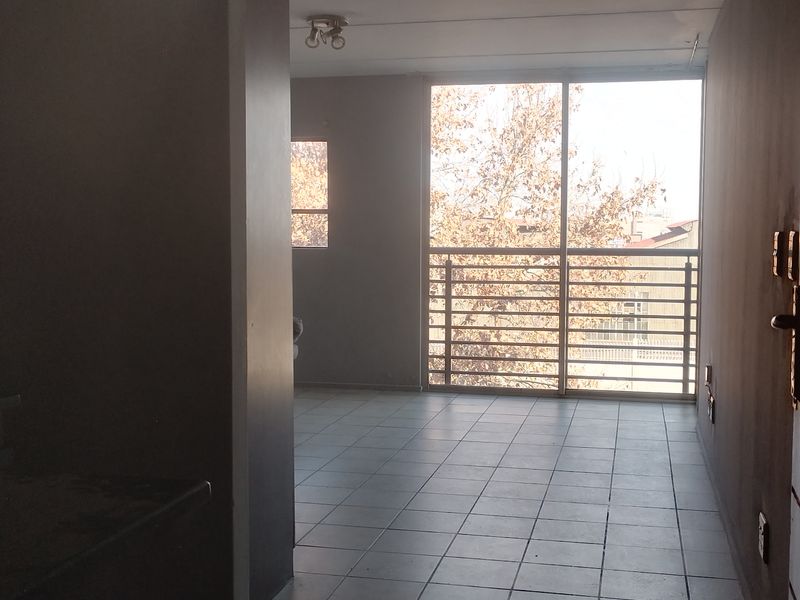 An empty living area featuring tiled flooring, a large sliding glass door leading to a balcony, and neutral wall finishes.