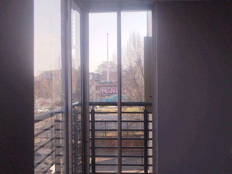 A simple balcony area featuring tiled flooring and a metal balustrade, accessible through a sliding glass door.
