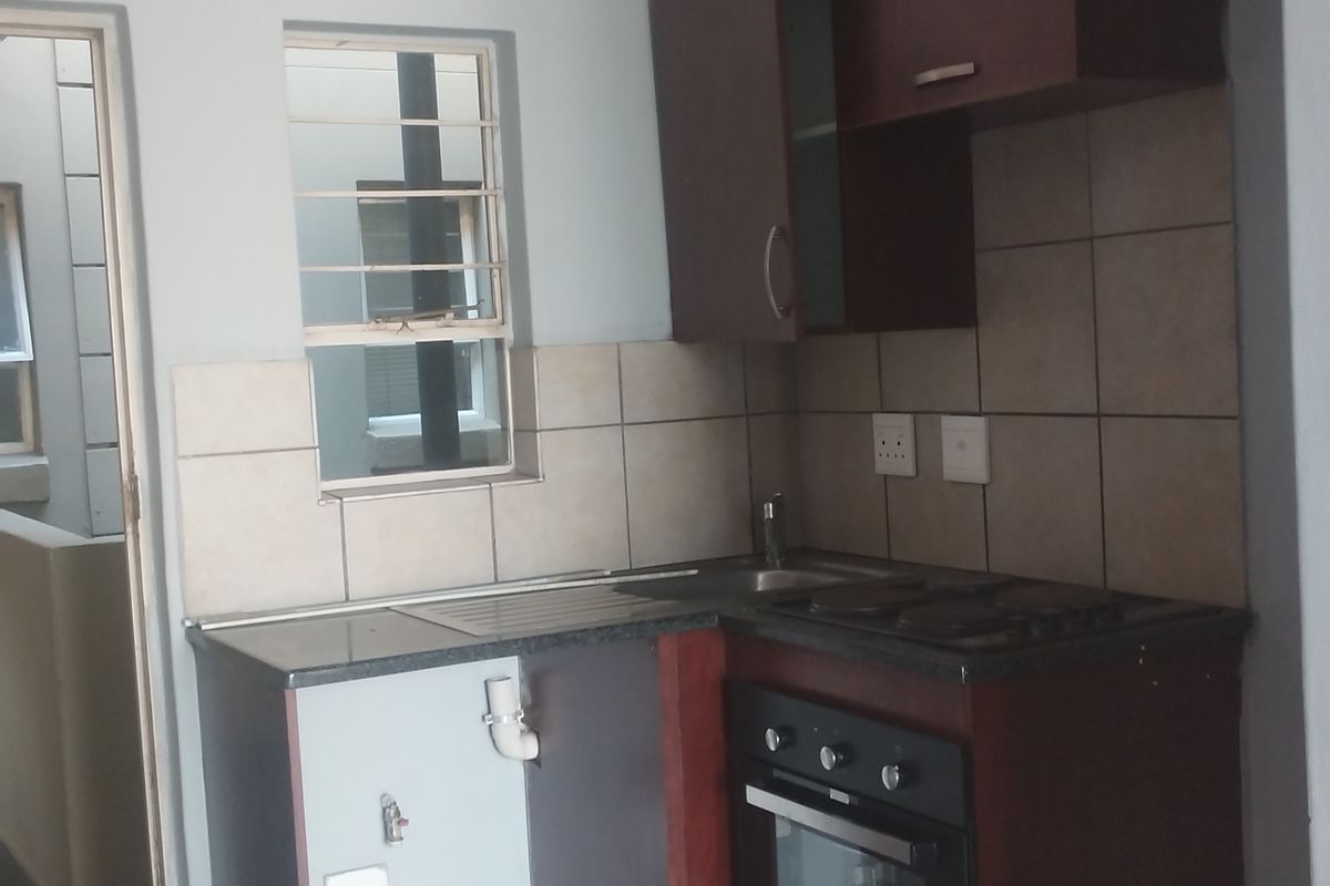Compact kitchen featuring dark wood cabinetry, granite countertops, built-in oven and hob, and tiled splashback, requiring minor repairs to cabinetry and plumbing.