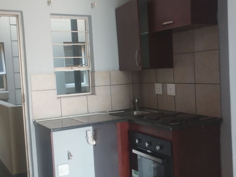 Compact kitchen featuring dark wood cabinetry, granite countertops, built-in oven and hob, and tiled splashback, requiring minor repairs to cabinetry and plumbing.
