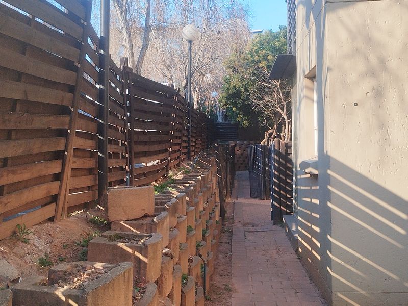 A narrow side passage featuring a paved walkway, timber slat fencing, and a tiered retaining wall structure along the side of the apartment building.