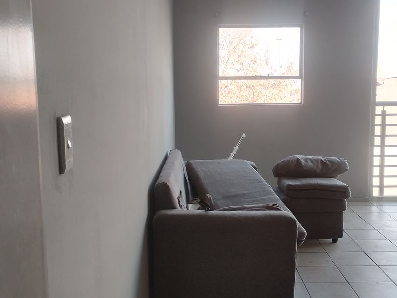 A simple living area featuring neutral walls, tiled flooring, and natural light from a window and sliding door access.