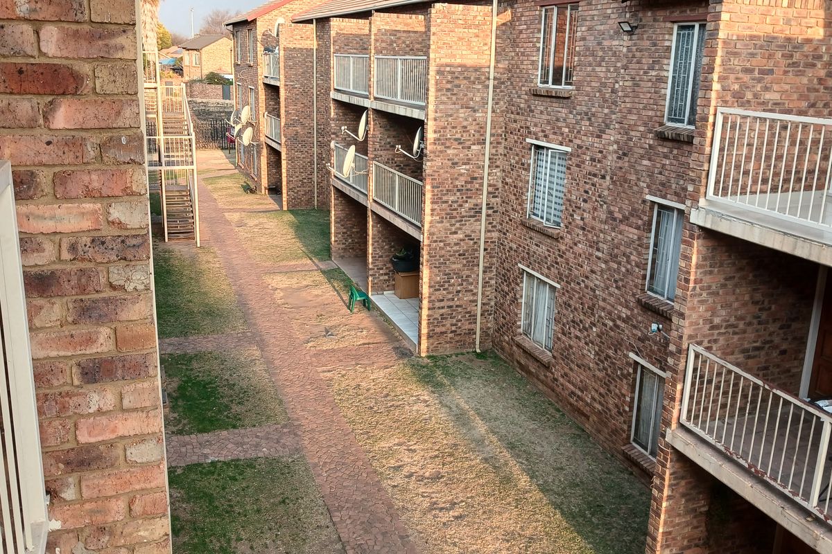 View of the rear exterior of a face brick townhouse complex featuring multiple balconies and a paved communal walkway.