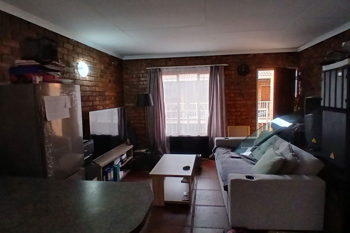 A living room featuring exposed brick walls and tiled flooring, with natural light entering through a window and an adjacent doorway.