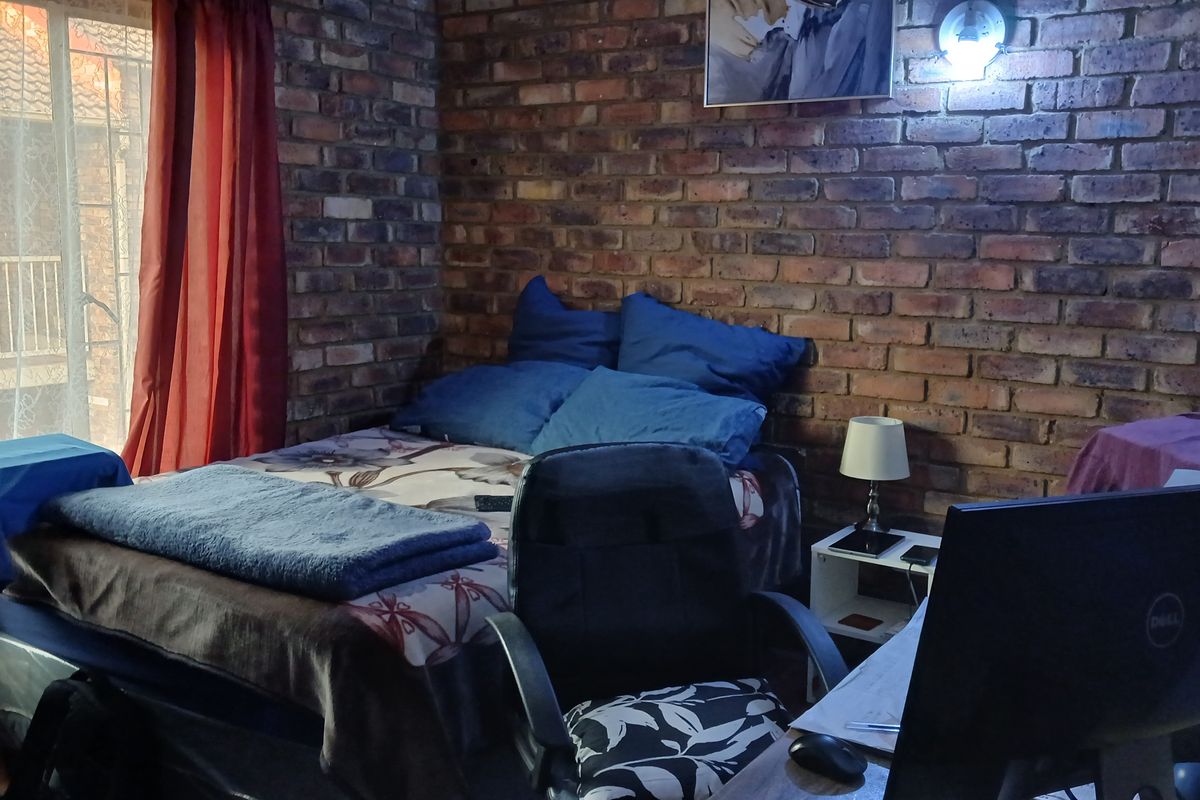 A bedroom featuring an exposed brick feature wall and a sliding glass door with security gate access to the exterior.