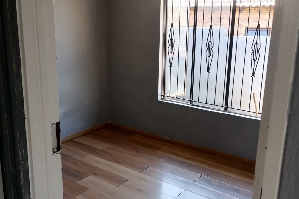 An empty bedroom featuring laminate flooring, a window with security bars, and a simple pendant light fixture.