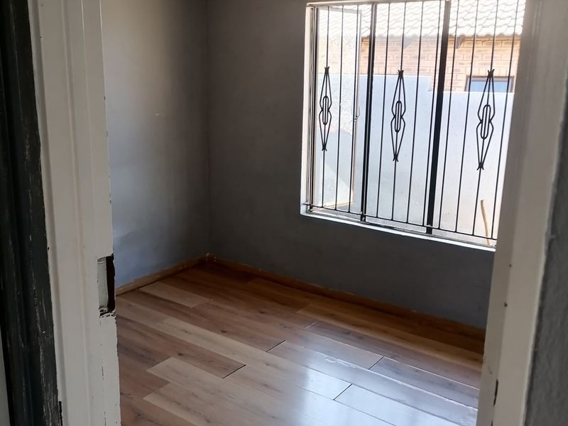 An empty bedroom featuring laminate flooring, a window with security bars, and a simple pendant light fixture.