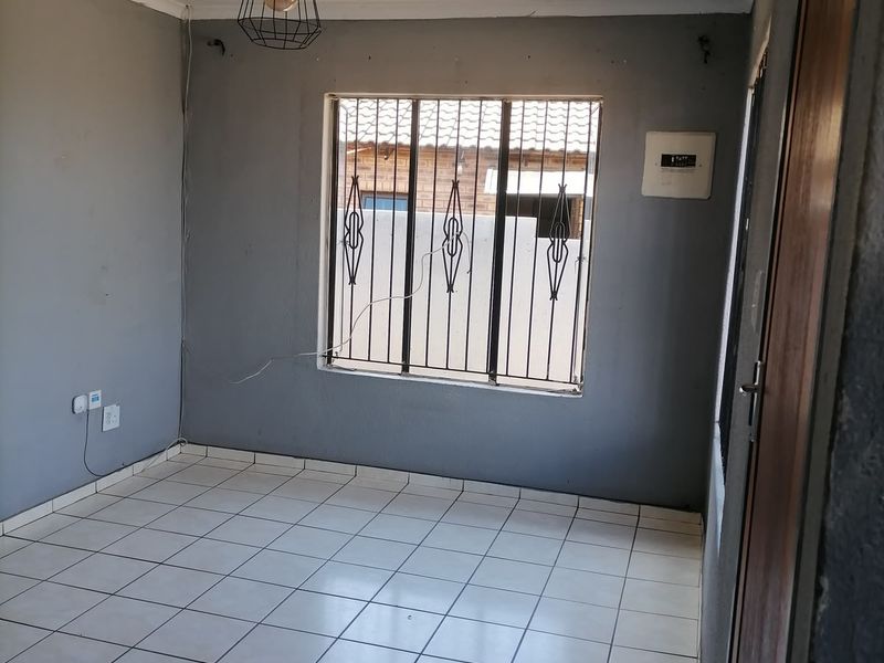 An empty living room featuring tiled flooring, security bars on the window, and a pendant light fitting, requiring minor cosmetic updates.