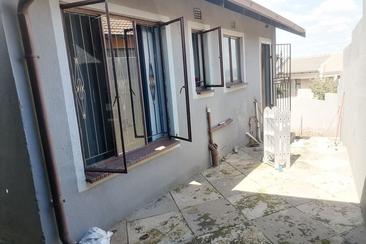 Rear exterior view of the property featuring paved patio area, security bars on windows, and exposed exterior plumbing.