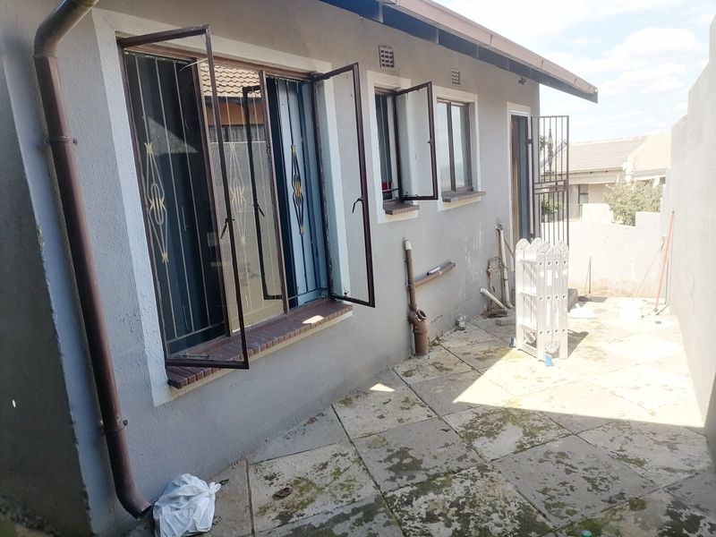 Rear exterior view of the property featuring paved patio area, security bars on windows, and exposed exterior plumbing.