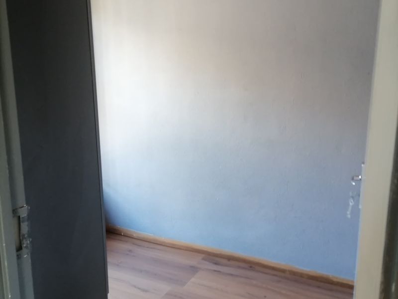 A clean, empty bedroom featuring modern laminate flooring, neutral grey walls, and a simple pendant light fixture.