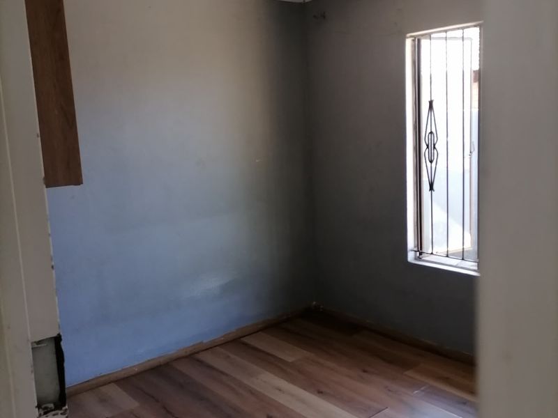 An empty bedroom featuring laminate flooring, grey painted walls, and a window fitted with security bars.