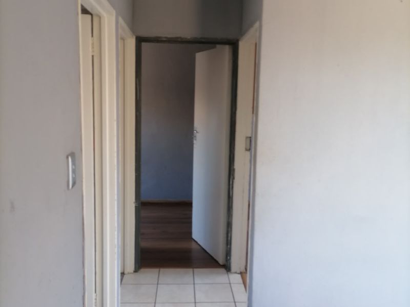 A vacant hallway featuring tiled flooring and grey painted walls, providing access to adjacent rooms through internal doorways.