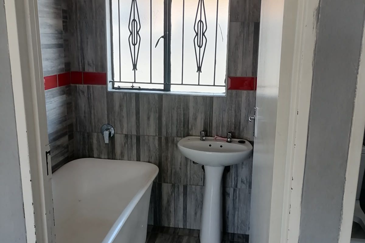 A compact bathroom featuring a pedestal basin, bathtub, and grey wood-look tiled walls with red accent tiles.