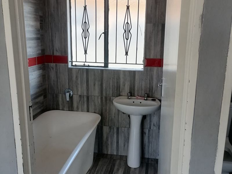 A compact bathroom featuring a pedestal basin, bathtub, and grey wood-look tiled walls with red accent tiles.