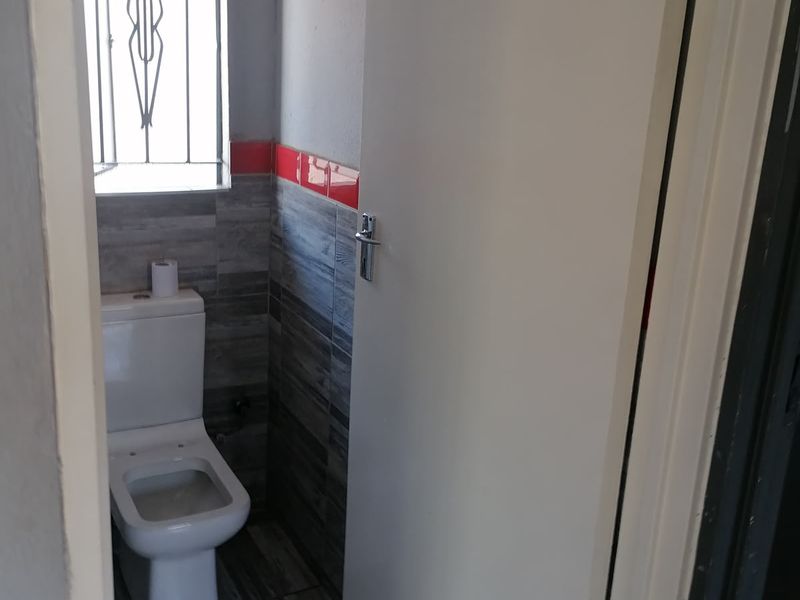 A compact bathroom featuring modern grey wood-look floor and wall tiles with a red accent border and a security-fitted window.