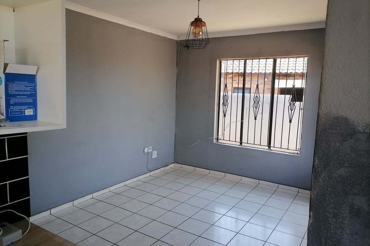 An empty living area featuring tiled flooring, security bars on the window, and a modern pendant light fixture.