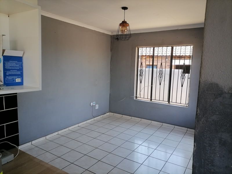 An empty living area featuring tiled flooring, security bars on the window, and a modern pendant light fixture.