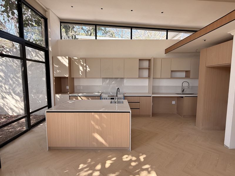 Modern, light-filled kitchen featuring a central island, light wood cabinetry, herringbone flooring, and expansive windows overlooking the garden.