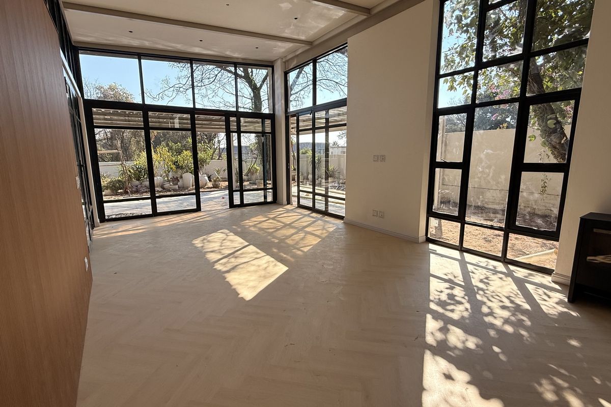 Spacious living area featuring expansive floor-to-ceiling windows, elegant herringbone timber flooring, and a modern built-in fireplace with abundant natural light.