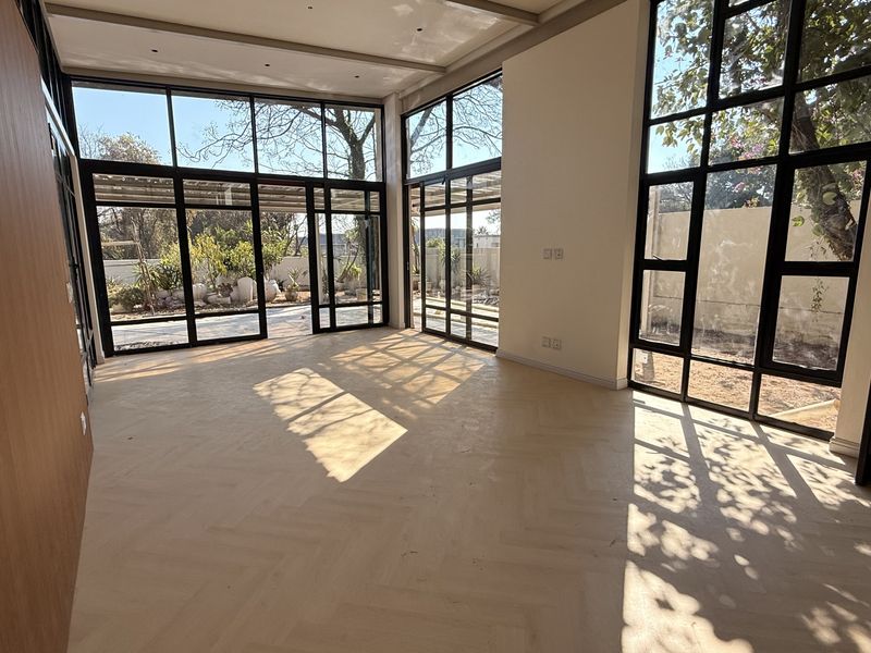 Spacious living area featuring expansive floor-to-ceiling windows, elegant herringbone timber flooring, and a modern built-in fireplace with abundant natural light.