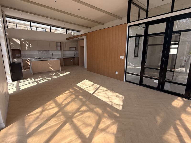 Spacious open-plan living and kitchen area featuring modern herringbone timber flooring, sleek cabinetry, and striking black steel-framed glass doors.