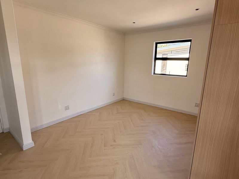 A bright, empty bedroom featuring modern herringbone flooring, neutral walls, and a built-in wardrobe, offering a clean canvas for personalization.