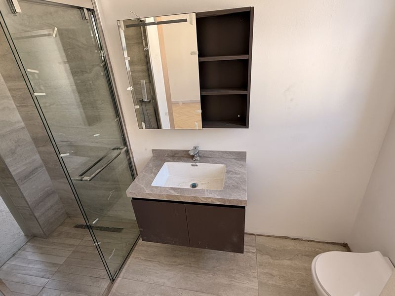 Modern bathroom featuring a glass-enclosed shower, wall-mounted vanity with stone countertop, and neutral tiling throughout. The space is clean and ready for final touches.