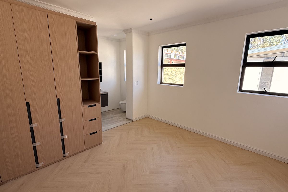 Spacious bedroom featuring light wood herringbone flooring, extensive built-in cabinetry, and direct access to an en-suite bathroom.