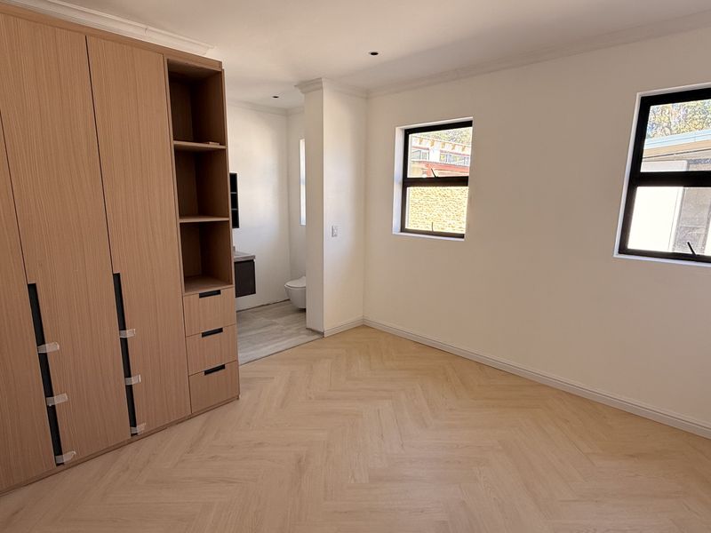 Spacious bedroom featuring light wood herringbone flooring, extensive built-in cabinetry, and direct access to an en-suite bathroom.